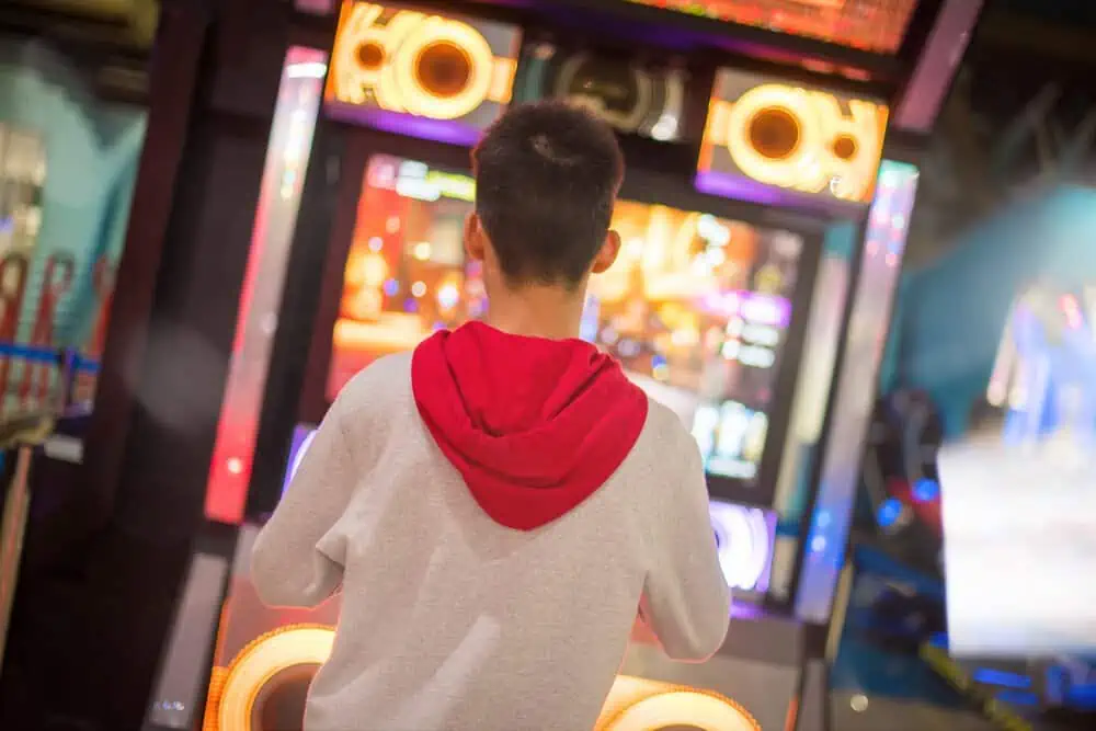 Young boy in sweater dancing with game arcade machine 